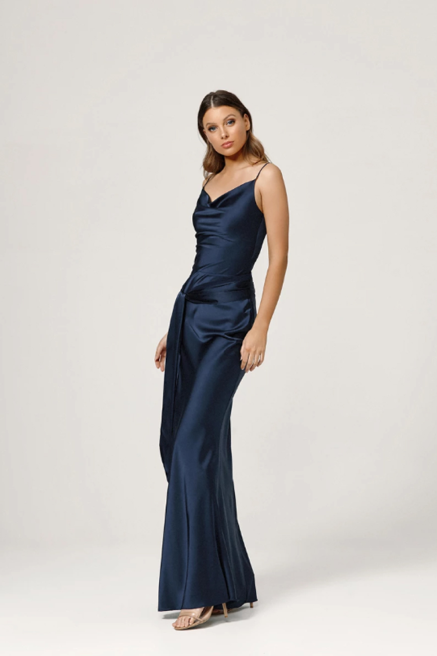 Model wearing Lexi Ashton navy cowl neck satin gown showing the left side of the dress